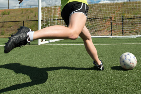 soccer player kicking a ball into the net