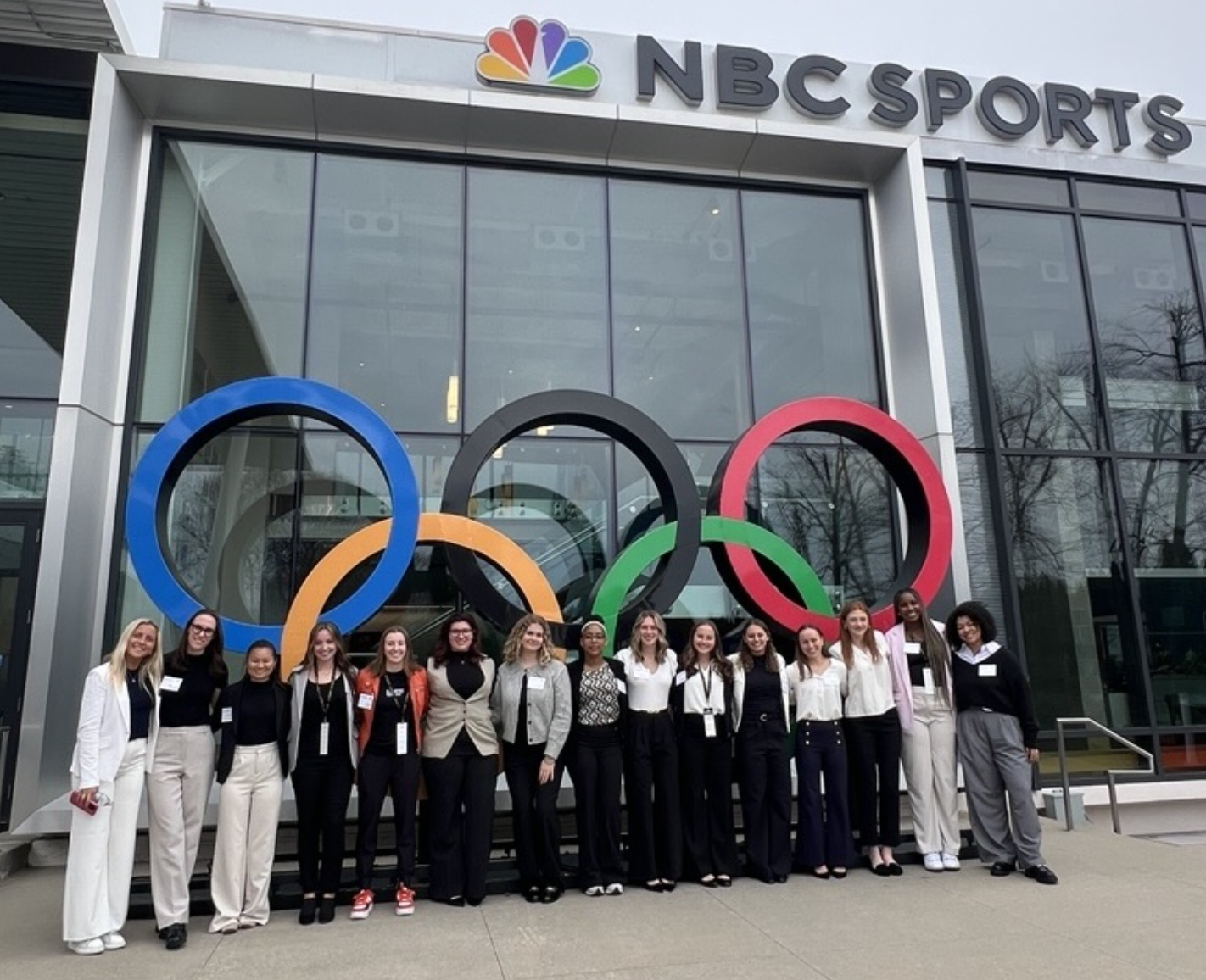 A group of college-aged women pose together in front of a building.