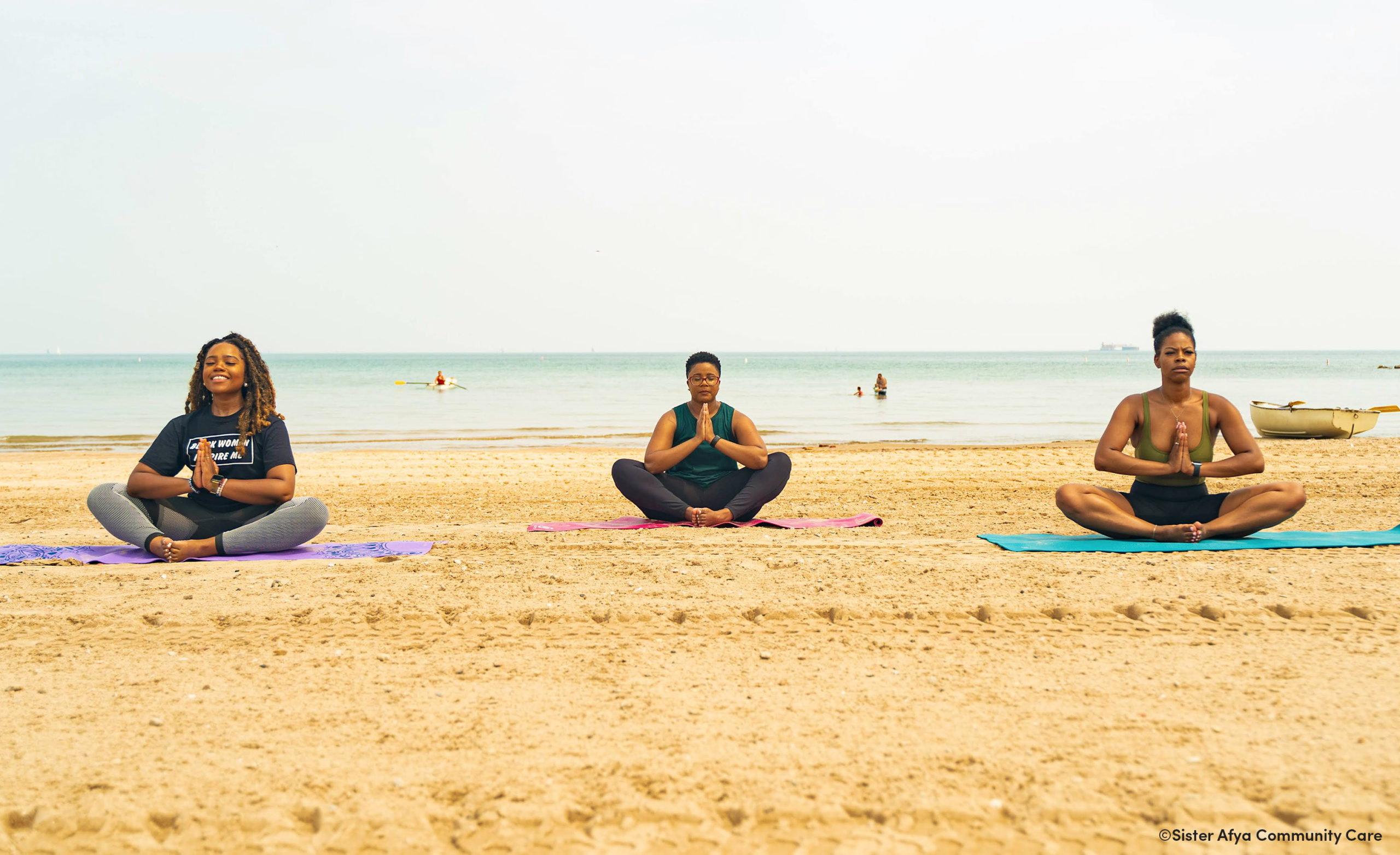 Photo of the Sister Afya Community Care program that shows three women of color in a yoga pose on the beach