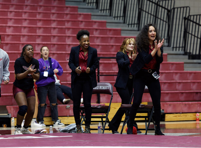 Three coaches at a wrestling match cheering on their athletes.
