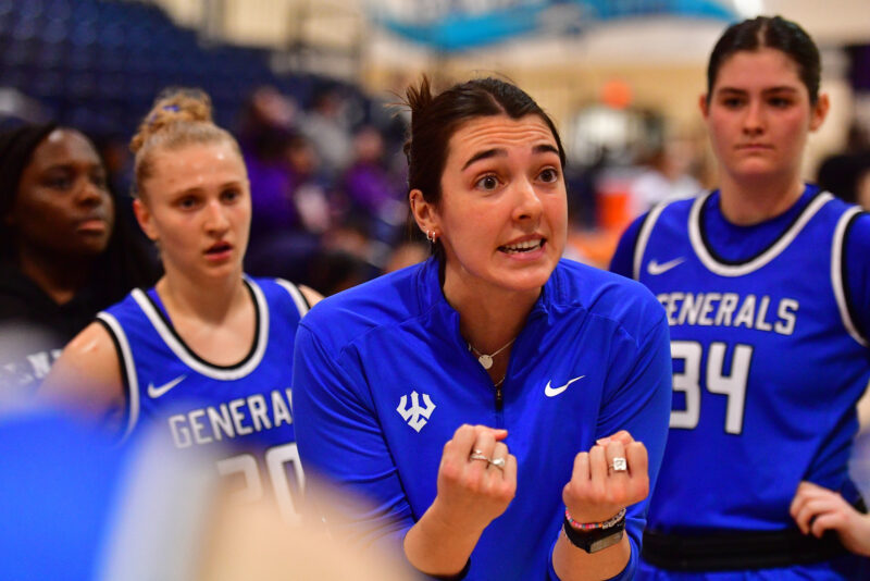 Female coach speaking passionately to players on sidelines of basketball game.