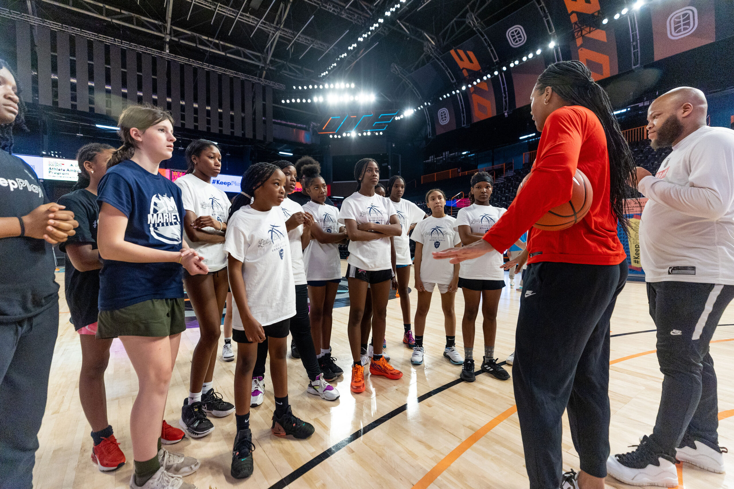 A group of girls gather in a huddle to listen to their basketball coach on the court