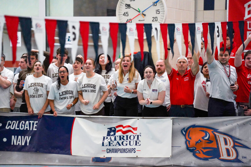 A group of coaches and athletes gather to cheer on teammates during a swim meet.