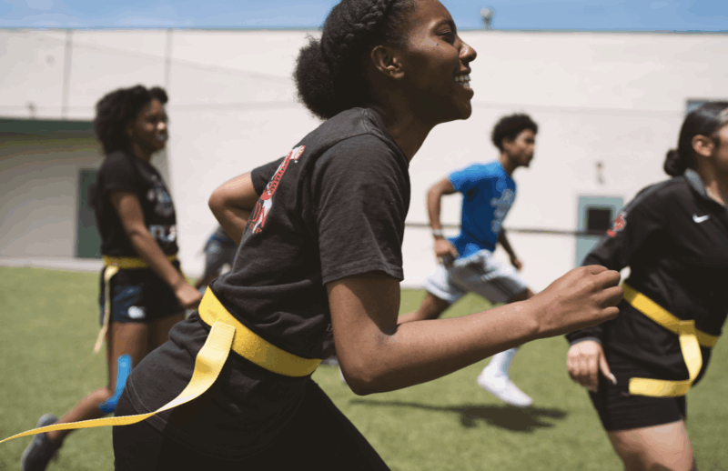 A girl smiling as she runs while playing flag football with friends.